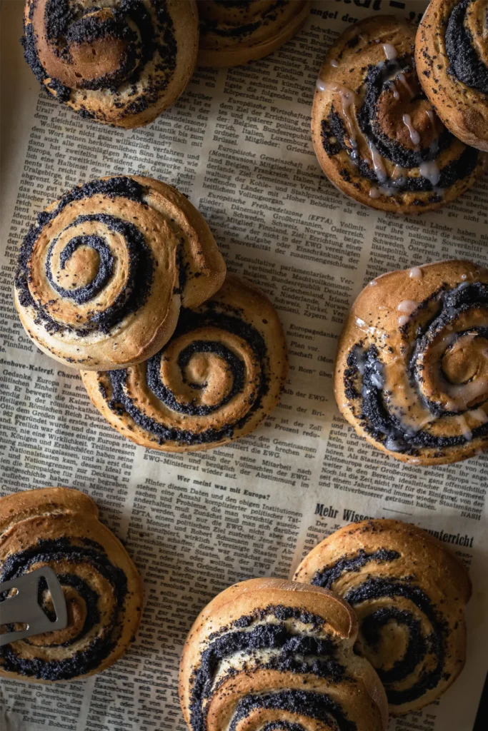 Goldbraune, frisch gebackene Mohnschnecken auf altem Zeitungspapier, fotografiert von David für Seiner Kochbackwelt – perfekt inszeniert für den Genussmoment.