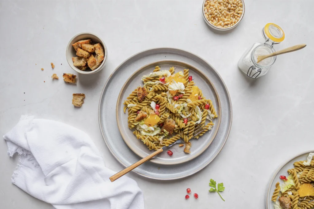 Winterlicher Erbsen-Fusilli-Salat mit Granatapfelkernen, Walnüssen, Orangenfilets, Pinienkernen und knusprigen Brotwürfeln, fotografiert von Kochbackwelt David Steiner.