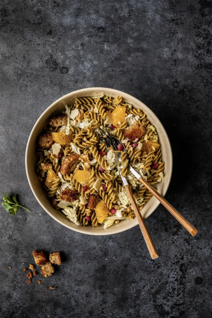 Winterlicher Erbsen-Fusilli-Salat mit Granatapfelkernen, Walnüssen, Orangenfilets, Pinienkernen und knusprigen Brotwürfeln, fotografiert von Kochbackwelt David Steiner.