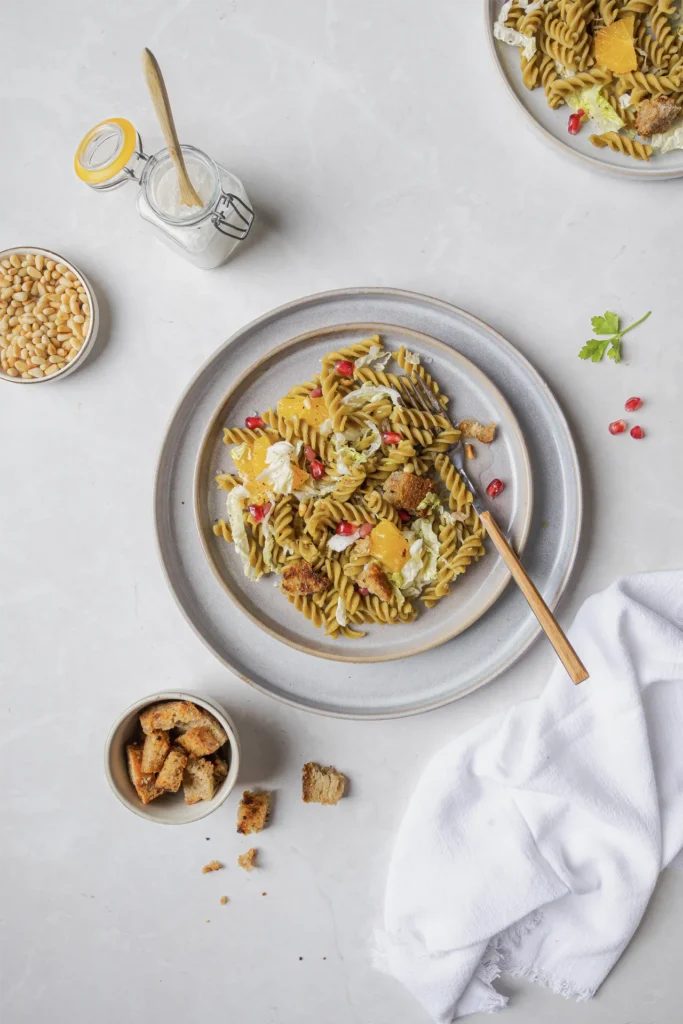 Winterlicher Erbsen-Fusilli-Salat mit Granatapfelkernen, Walnüssen, Orangenfilets, Pinienkernen und knusprigen Brotwürfeln, fotografiert von Kochbackwelt David Steiner.