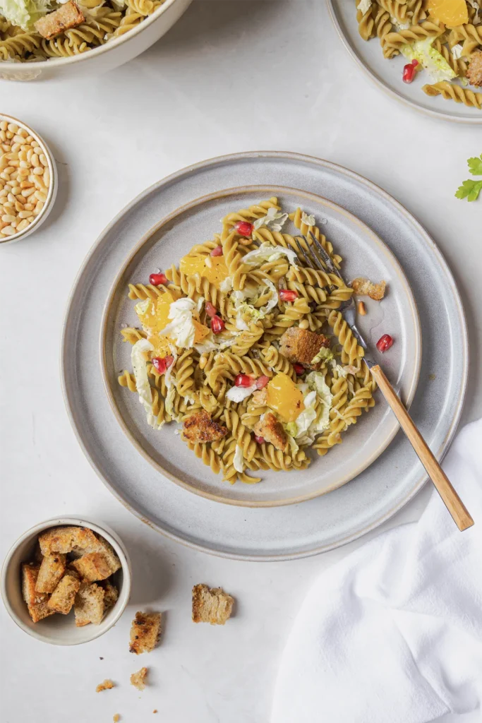 Winterlicher Erbsen-Fusilli-Salat mit Granatapfelkernen, Walnüssen, Orangenfilets, Pinienkernen und knusprigen Brotwürfeln, fotografiert von Kochbackwelt David Steiner.