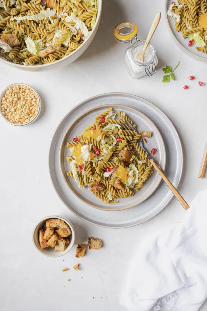 Winterlicher Erbsen-Fusilli-Salat mit Granatapfelkernen, Walnüssen, Orangenfilets, Pinienkernen und knusprigen Brotwürfeln, fotografiert von Kochbackwelt David Steiner.