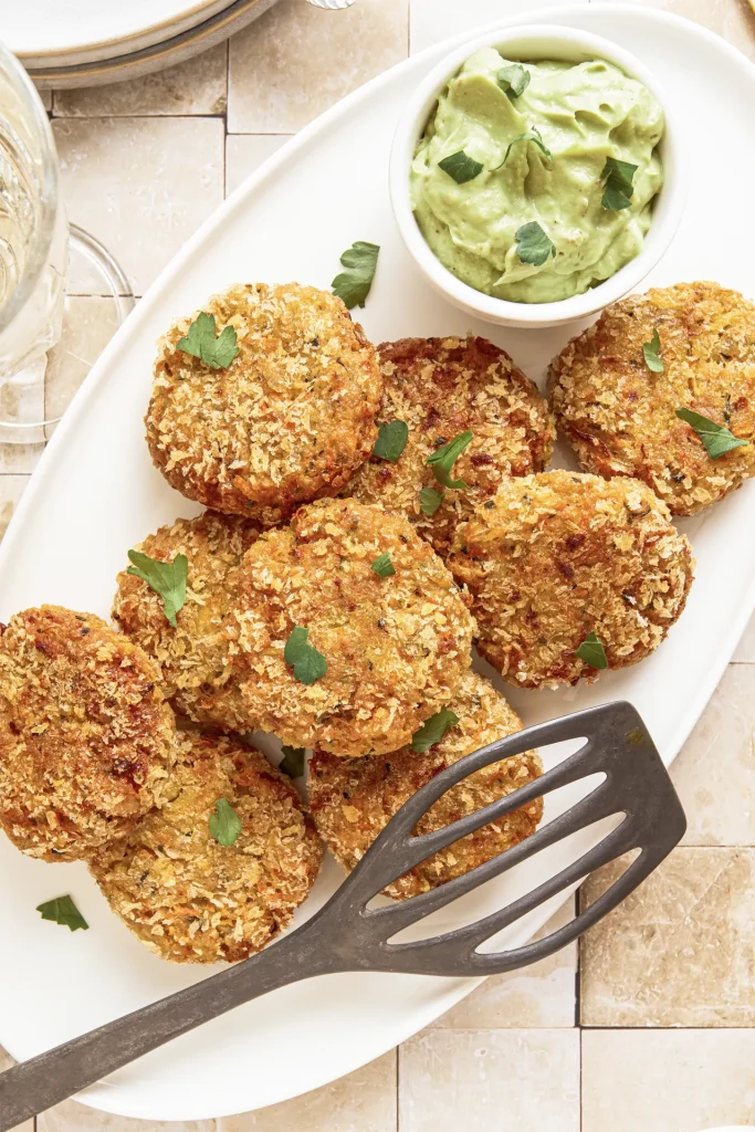 Gemüse-Bratlinge mit Avocado-Tahini-Dip, inspiriert von der Levante-Küche, serviert auf einem Teller mit frischen Kräutern und orientalischen Aromen.