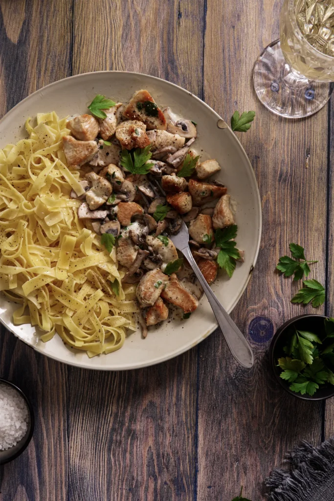 Puten-Geschnetzeltes mit Champignons in cremiger Sauce, serviert mit Bandnudeln auf einem Teller, garniert mit frischer Petersilie.