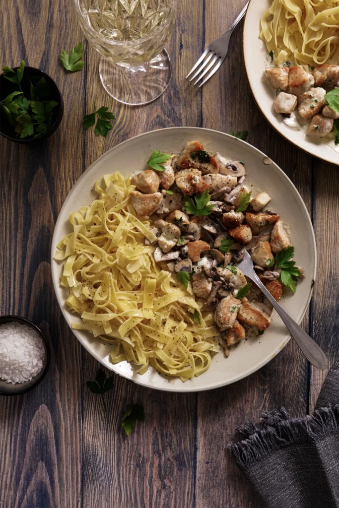 Puten-Geschnetzeltes mit Champignons in cremiger Sauce, serviert mit Bandnudeln auf einem Teller, garniert mit frischer Petersilie.