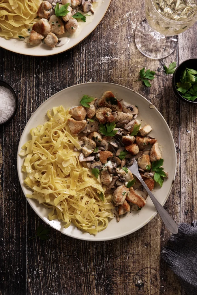 Puten-Geschnetzeltes mit Champignons in cremiger Sauce, serviert mit Bandnudeln auf einem Teller, garniert mit frischer Petersilie.